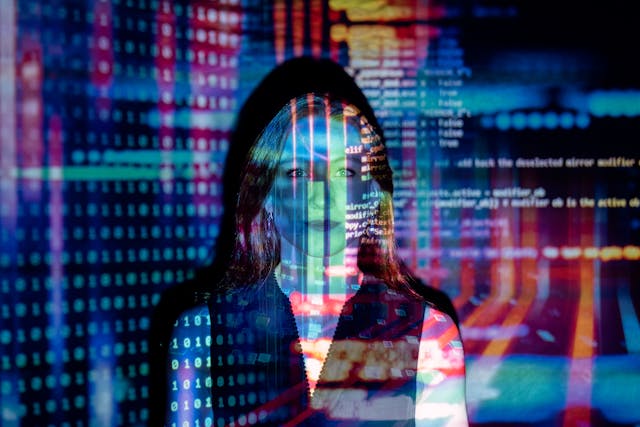 Des codes informatiques colorés projetés sur une femme dans une pièce sombre.
