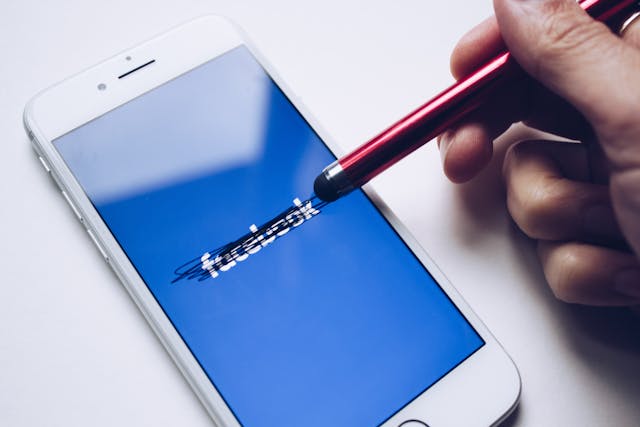 스타일러스 펜으로 휴대폰의 Facebook 로고를 지우고 있는 사람.