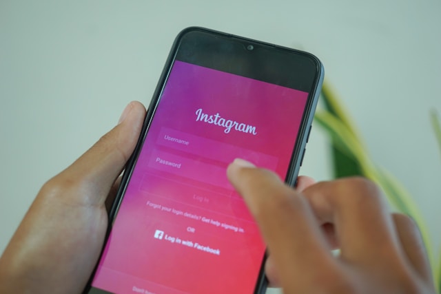 Someone holding their phone, which displays the pink Instagram login page.