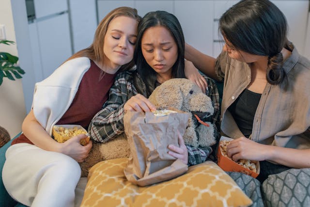 Dos mujeres consuelan a su triste amiga mientras comen palomitas juntas.