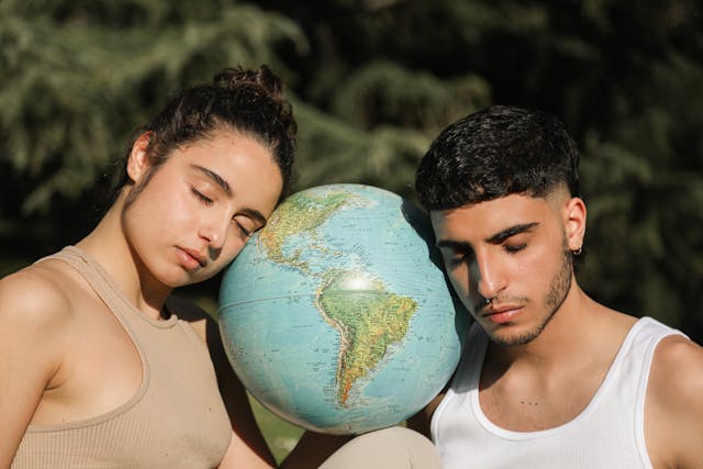 Um homem e uma mulher de olhos fechados apoiam a cabeça num globo terrestre.