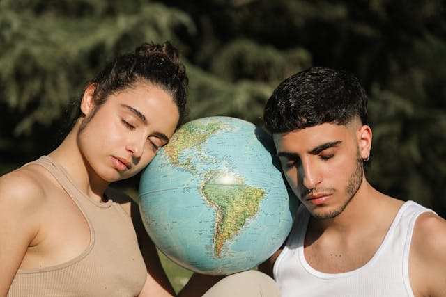 Un uomo e una donna con gli occhi chiusi appoggiano la testa su un mappamondo.