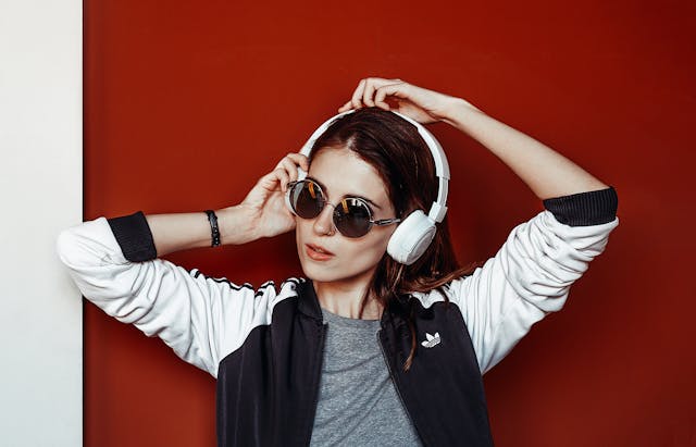 A woman with sunglasses adjusting her white headphones while listening to music.