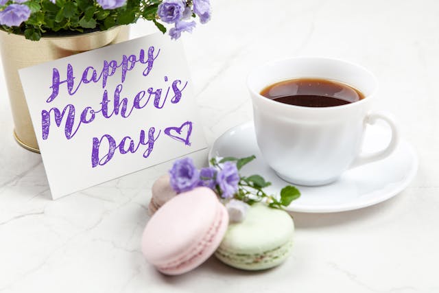Eine Tasse Tee und ein Teller mit Macarons auf einem Tisch neben einem Zettel mit der Aufschrift "Alles Gute zum Muttertag".