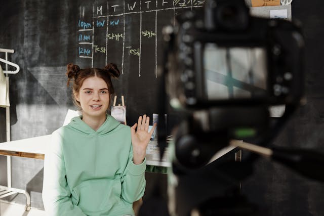 Uma criadora de conteúdos acena para a câmara enquanto filma uma publicação de vídeo introdutória.