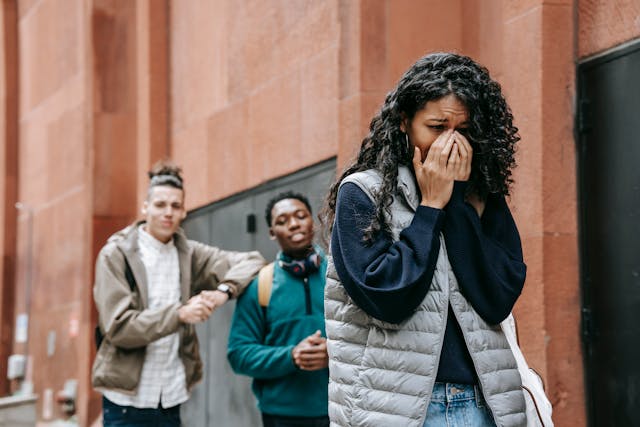 Una giovane donna che piange mentre i suoi compagni di classe maschi dicono cose sconce alle sue spalle