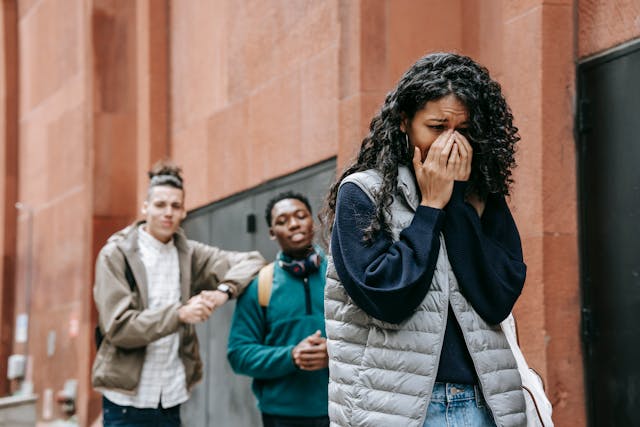 Uma jovem mulher a chorar enquanto os seus colegas de turma dizem coisas desagradáveis atrás dela