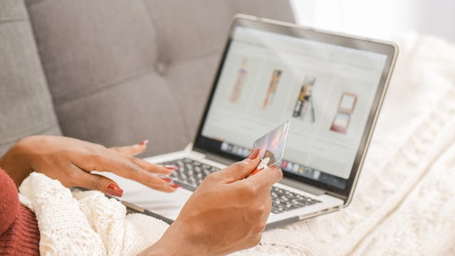 Una persona che naviga in un negozio online sul suo computer portatile mentre ha in mano una carta di credito.