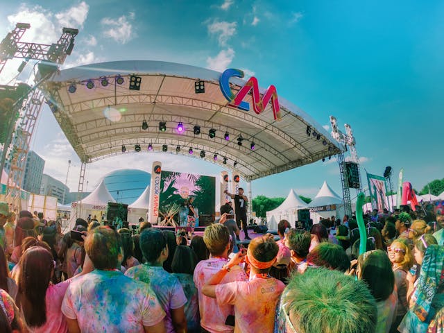 Une foule de personnes aux cheveux et aux vêtements tachés de peinture se tenant devant une scène de concert lors d'un festival.