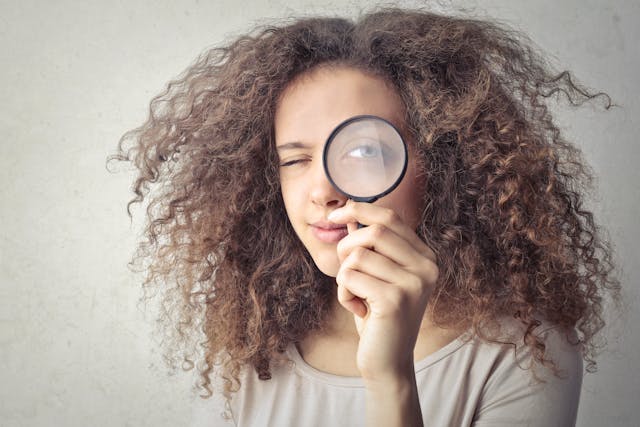 Una donna con i capelli ricci che tiene una lente d'ingrandimento vicino all'occhio.