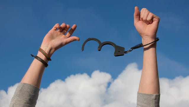 A man holding his hands up at the sky with uncuffed handcuffs.