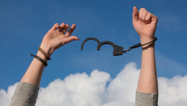 Un homme qui lève les mains vers le ciel avec des menottes non attachées.