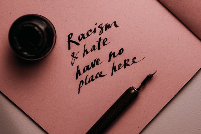 Un stilou lângă un bilet scris de mână pe care scrie: &quot;Rasismul și ura nu-și au locul aici&quot;.