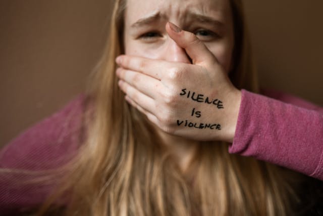 Een meisje bedekt haar mond met haar hand, waarop "Stilte is geweld" staat geschreven.