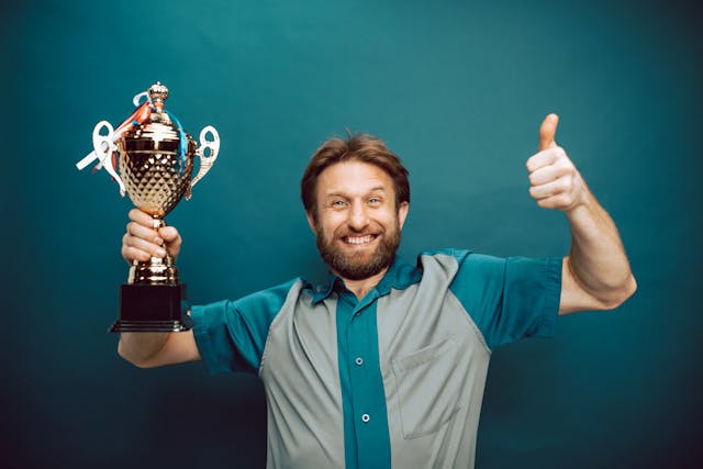 Een lachende man die met één hand een trofee vasthoudt en met de andere duim omhoog steekt.