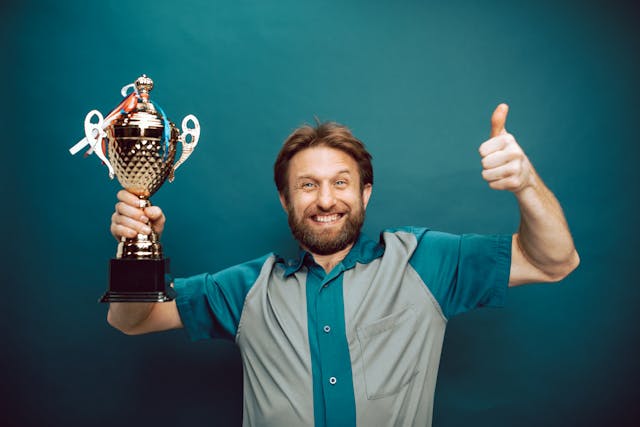 Ein lächelnder Mann, der mit einer Hand eine Trophäe hält und mit der anderen den Daumen nach oben streckt.