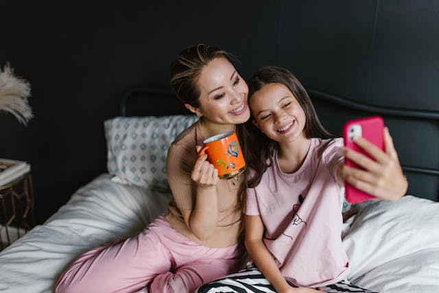 Een klein meisje neemt een selfie met haar moeder in hun slaapkamer.