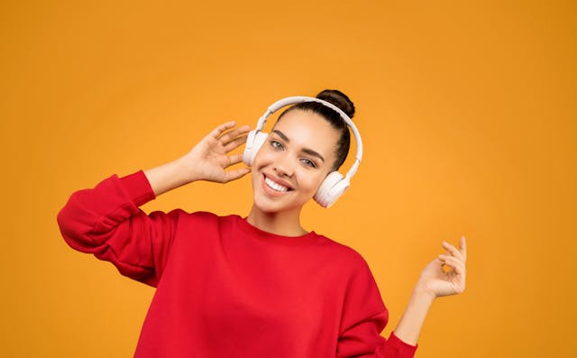 A woman in a red sweater smiling while listening to music using headphones.
