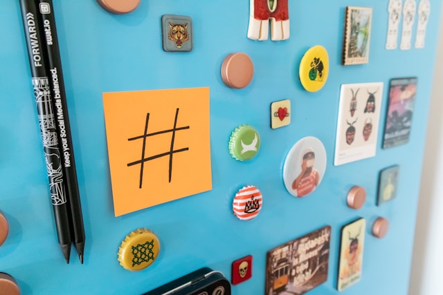 Een blauw prikbord met een sticky note met het hashtag-symbool en kleurrijke spelden en flessendoppen.