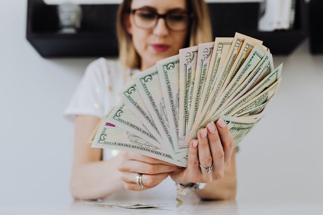 pexels-karolina-grabowska-4968652 | Path Social A woman looking at a fan of dollar bills she’s holding.