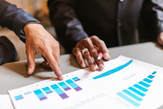 pexels-rdne-8068694 | Path Social Two men’s hands pointing to data charts and graphs on a piece of paper on an office table.
