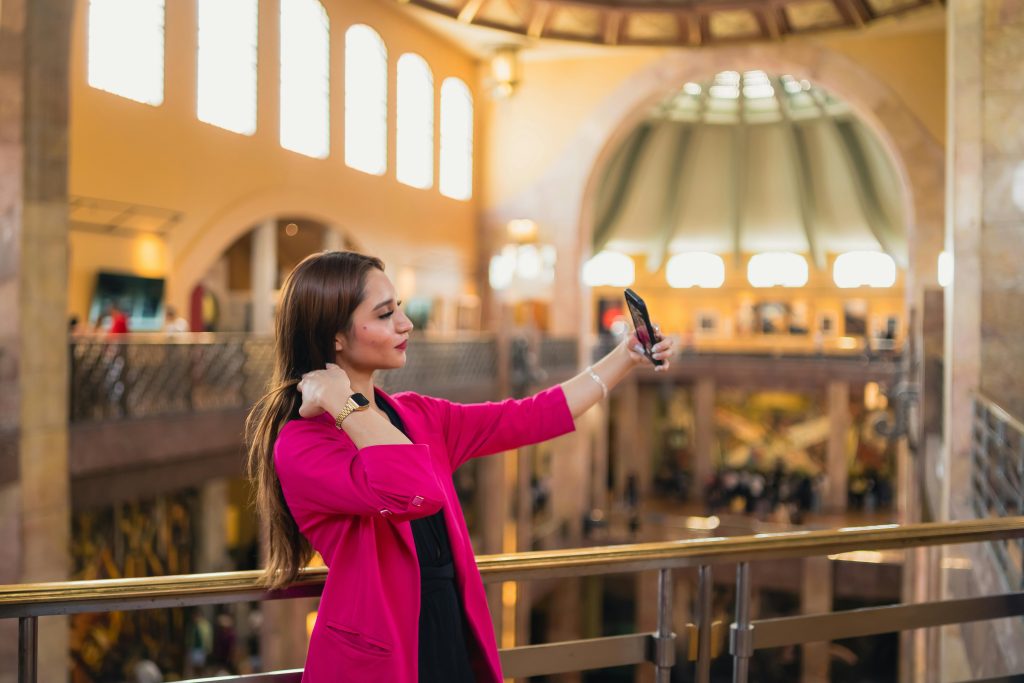 pexels-julio-lopez-75309646-20527039 | Path Social Eine Frau in einem pinkfarbenen Blazer macht ein Selfie mit ihrem Handy.