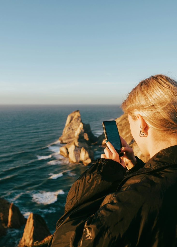 pexels-kokorevas-14683098 | Path Social Eine blonde Frau, die ein Panoramafoto von Felsen im Meer macht.