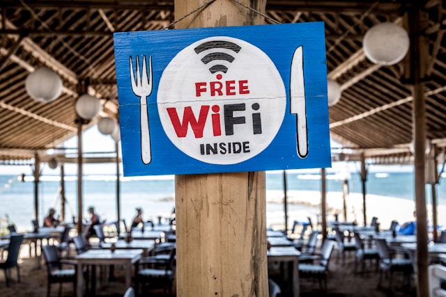 Um sinal "Wi-Fi grátis no interior" desenhado à mão num poste de madeira no exterior de um restaurante à beira-mar.