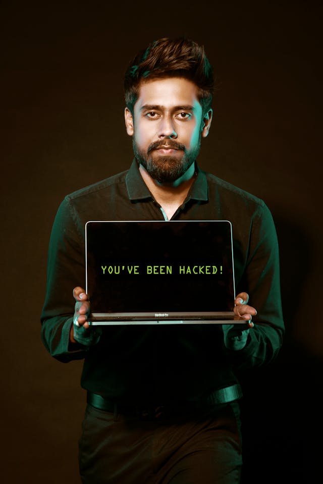 Um homem segura um computador portátil com as palavras "You've been hacked!" no ecrã.