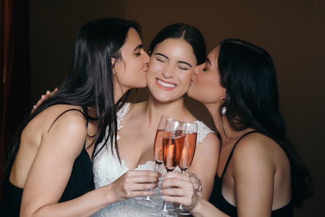 pexels-cristian-rojas-8459369 | Path Social シャンパンのグラスを手に、女性の頬にキスをする2人の女友達。
