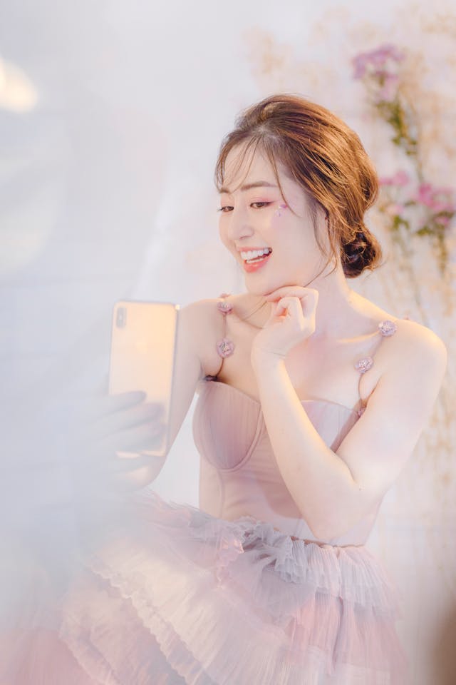 pexels-hson-12488303 | Path Social スマートフォンを見ながら微笑むピンクのチュールドレスを着た女性。