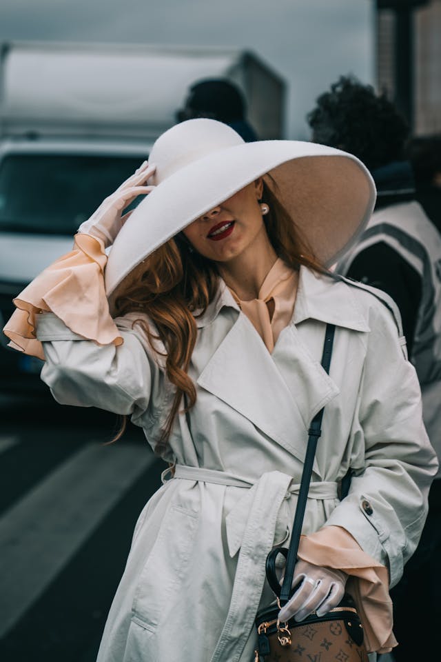 pexels-toniimal-28751191 | Path Social トレンチコートに手袋をはめ、ふわふわの白い帽子で顔を覆った洗練された女性。