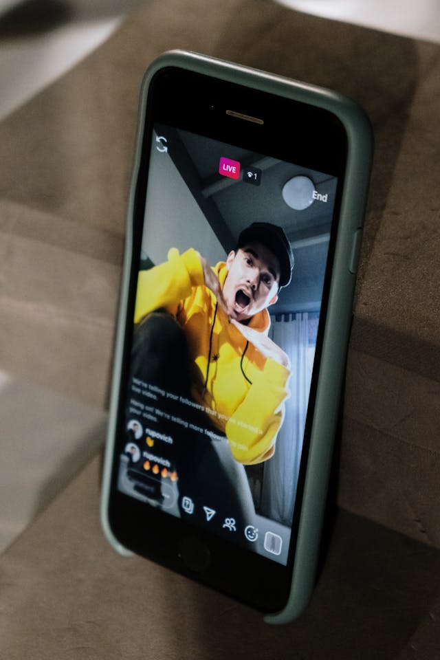 노란 후드티를 입은 남성이 스마트폰으로 Instagram 라이브 방송을 하고 있습니다.