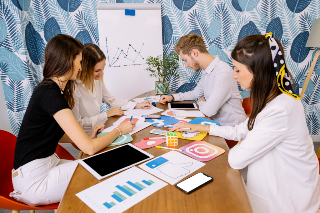 A group of people working on social media marketing with charts, tablets, and logo cutouts on the table.